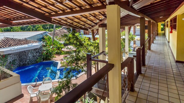 A covered outdoor area with a swimming pool, a stone wall, and a tiled floor. - Chaua Porto Hotel (Porto Seguro)
