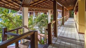 A covered outdoor corridor with tiled flooring, wooden railings, and a view of greenery and buildings in the background. - Chaua Porto Hotel (Porto Seguro)