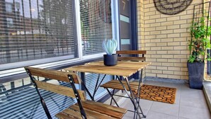 Een terras met een houten tafel en stoelen, een plant in pot en een deur met het nummer 7.
