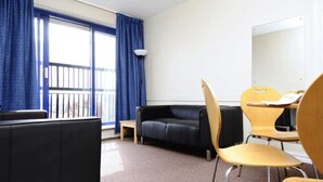 Ein Hotelzimmer mit einer schwarzen Ledersofa, Holzstühlen, einem kleinen Tisch und einem großen Fenster mit blauen Vorhängen.