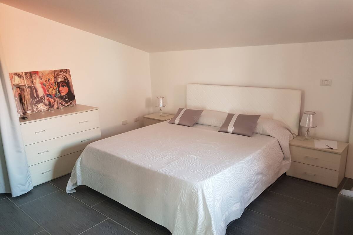 Une chambre à coucher avec un grand lit, une commode, une table de chevet, une lampe et un tableau au mur.