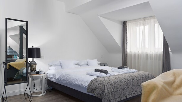 A modern bedroom with a large bed, a bedside table with a lamp, a mirror, and a window with curtains. - Trip Inn Boutique Rubens Essen (Essen)