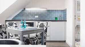 A compact kitchen with a modern design, featuring a black and white patterned chair, a glass-top table, and a blue tiled backsplash. - Trip Inn Boutique Rubens Essen (Essen)