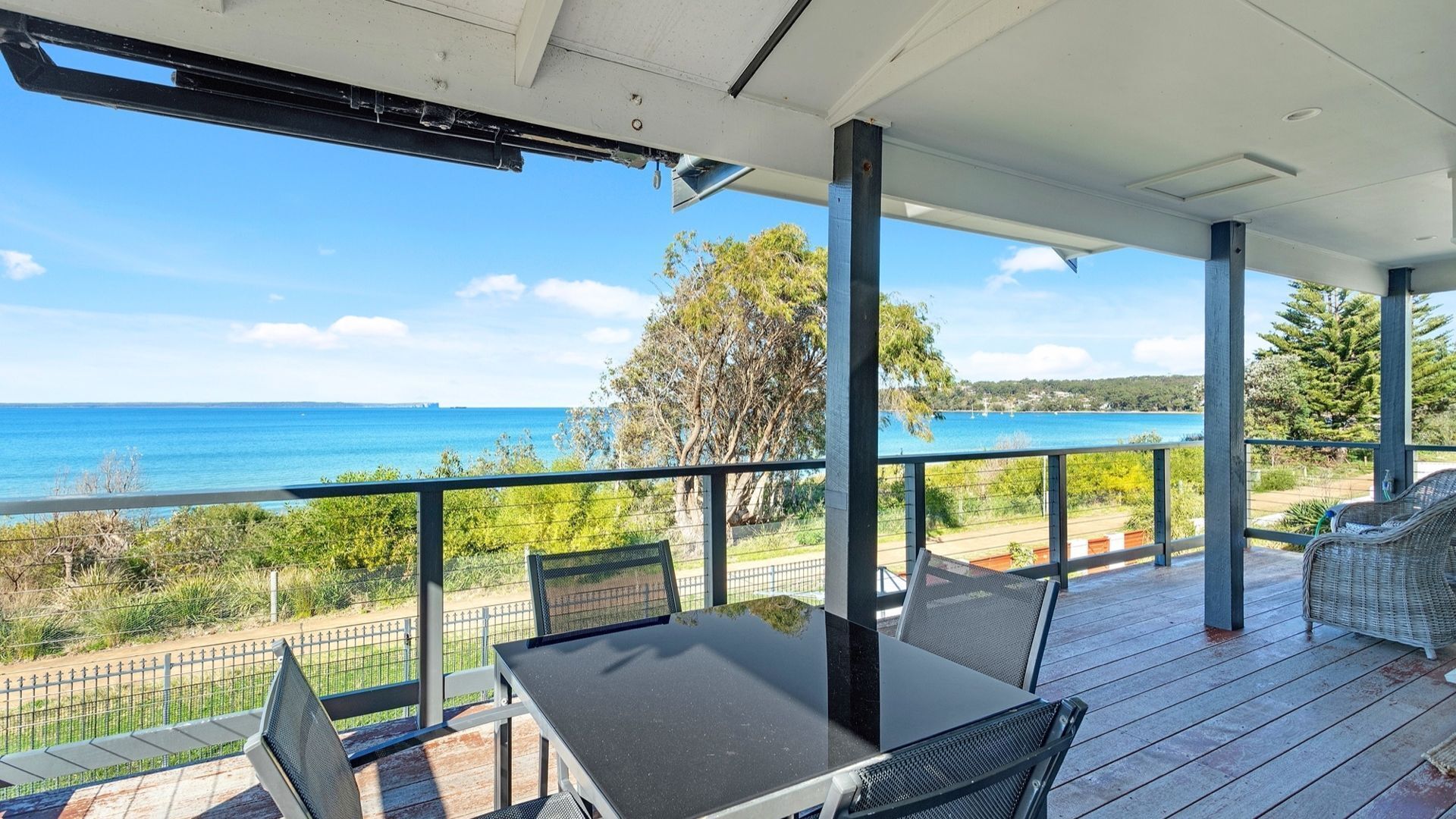 A covered outdoor area with a table and chairs, overlooking a coastal view.