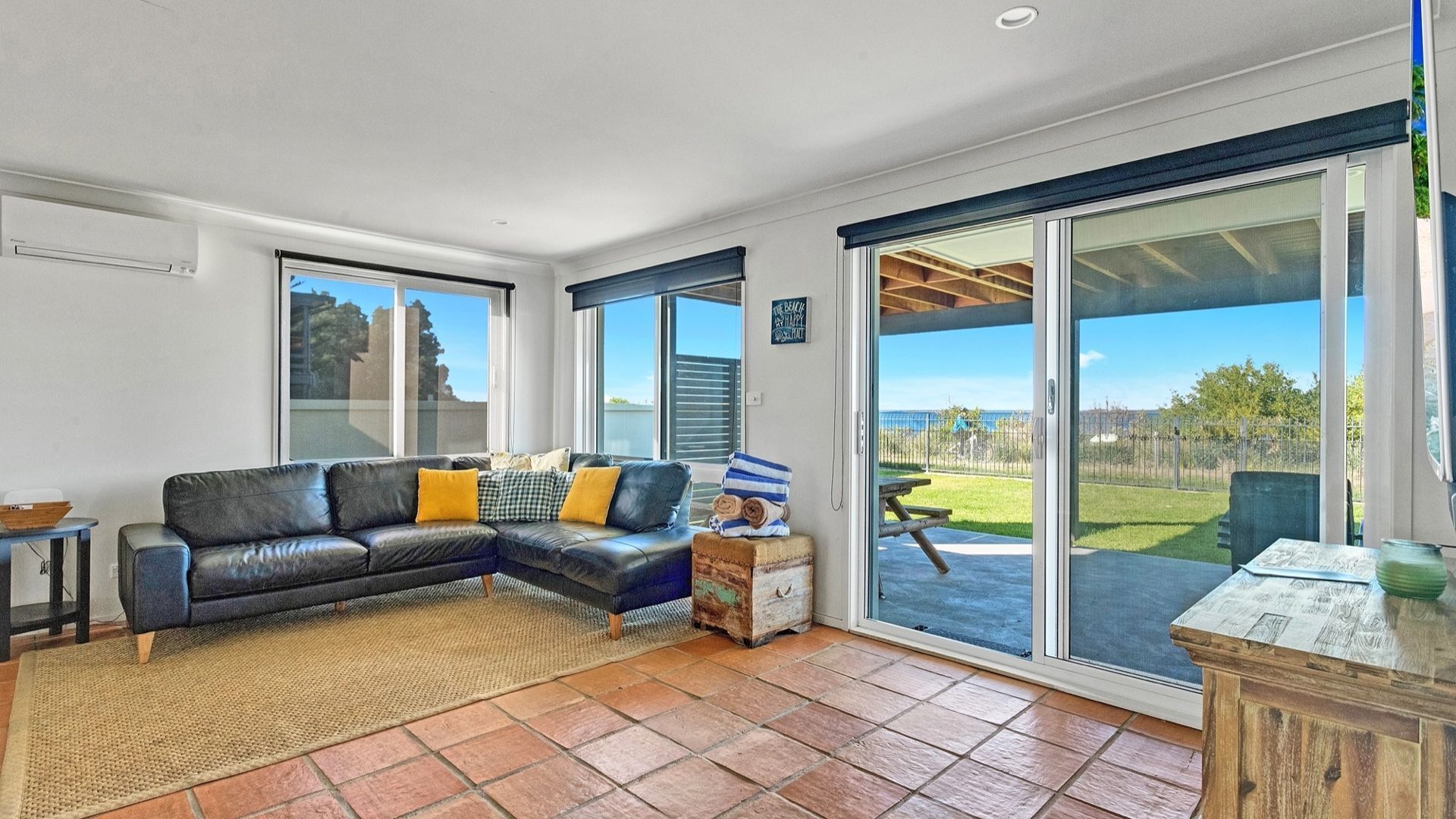 A spacious living room with a leather sofa, large windows, and a view of a backyard.