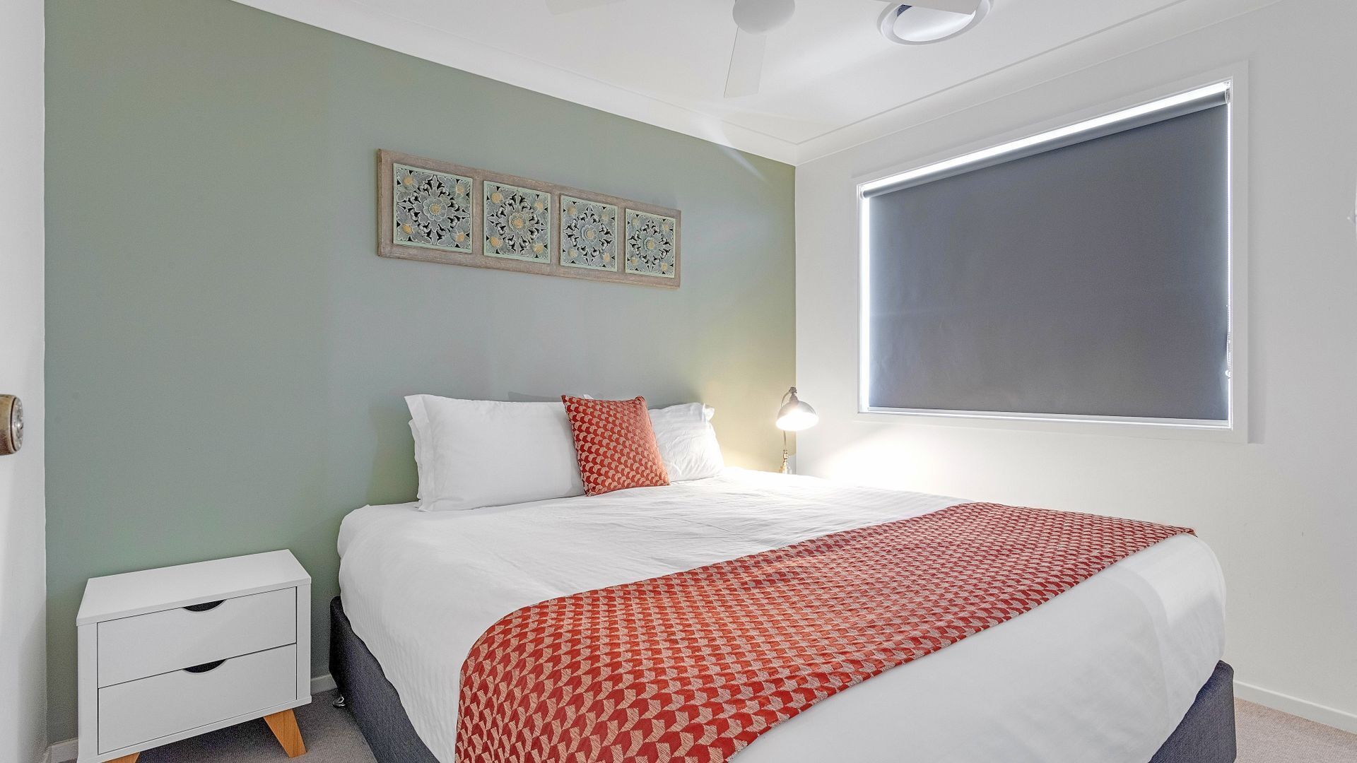 A bedroom with a bed, a nightstand, a lamp, and a window with blinds.