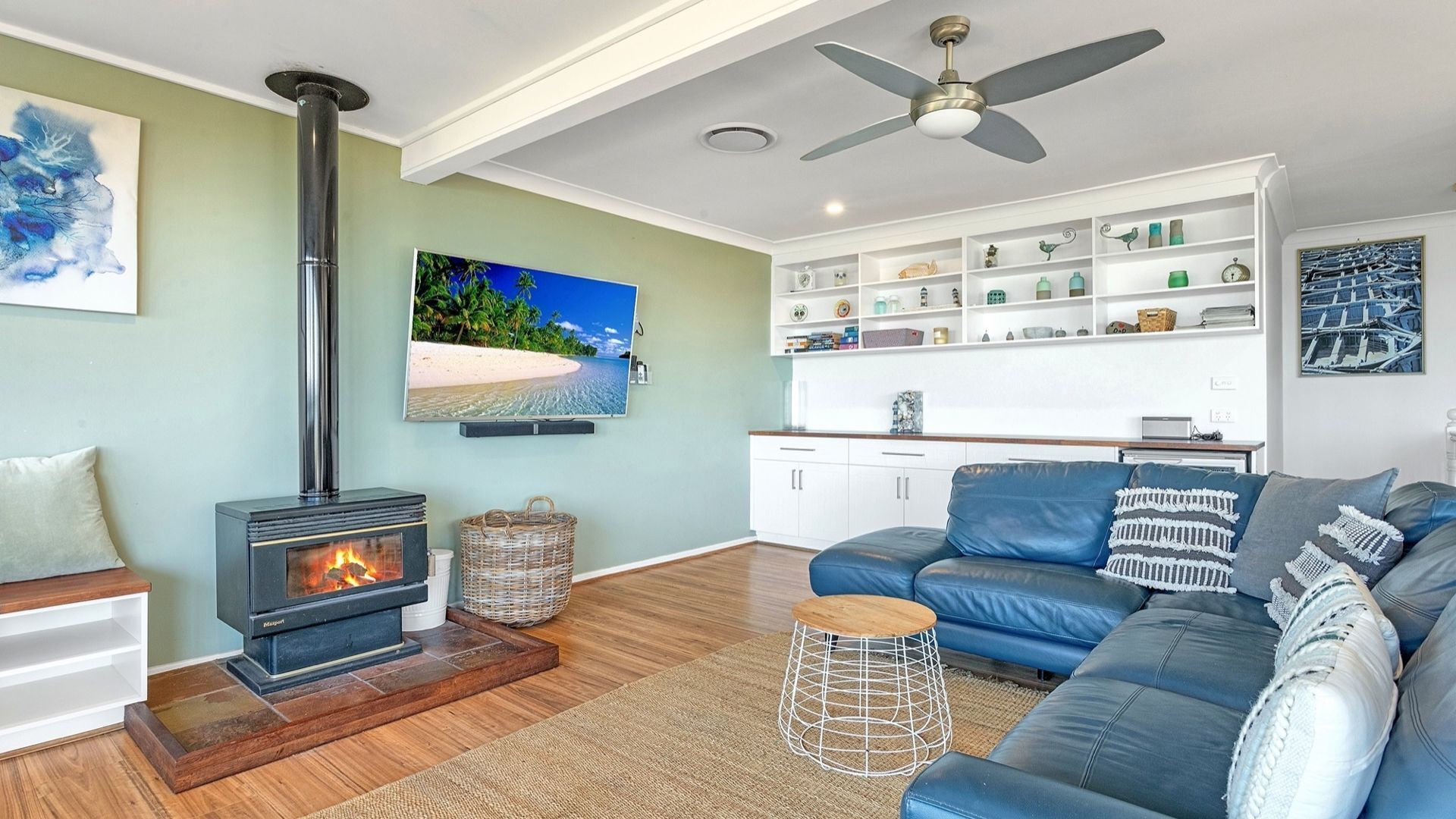 A living room with a wood-burning stove, a blue sofa, a television, and a ceiling fan.