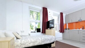 A bedroom with a bed, a television, and a window with curtains. - Wood Green Hall - Campus Accommodation (London)