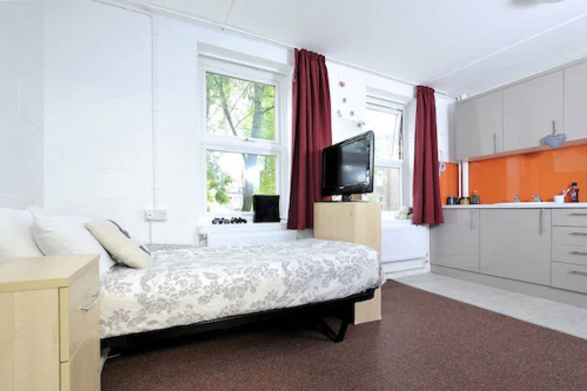 A bedroom with a bed, a television, and a window with curtains.