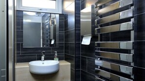 A modern bathroom with a large mirror, a sink, and a wall-mounted towel dispenser. - Wood Green Hall - Campus Accommodation (London)