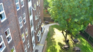 A high-rise building with multiple windows and a small courtyard with a tree and benches. - Wood Green Hall - Campus Accommodation (London)