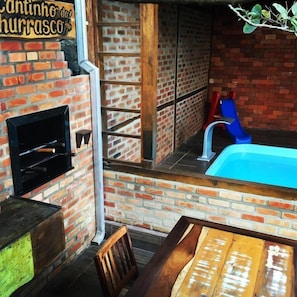 A brick wall with a grill, a blue pool, and a slide.