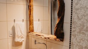 A bathroom with a wooden vanity, a glass sink, a mirror with a wooden frame, and a toilet. - Pousada Armação das Baleias (Penha)