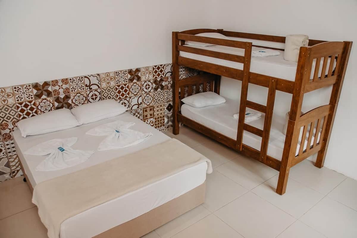 A bunk bed with a wooden frame and white bedding, a patterned tile wall, and a plain white floor.