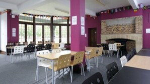 A library with tables and chairs, a fireplace, and large windows. - Platt Hall - Campus Accommodation (London)