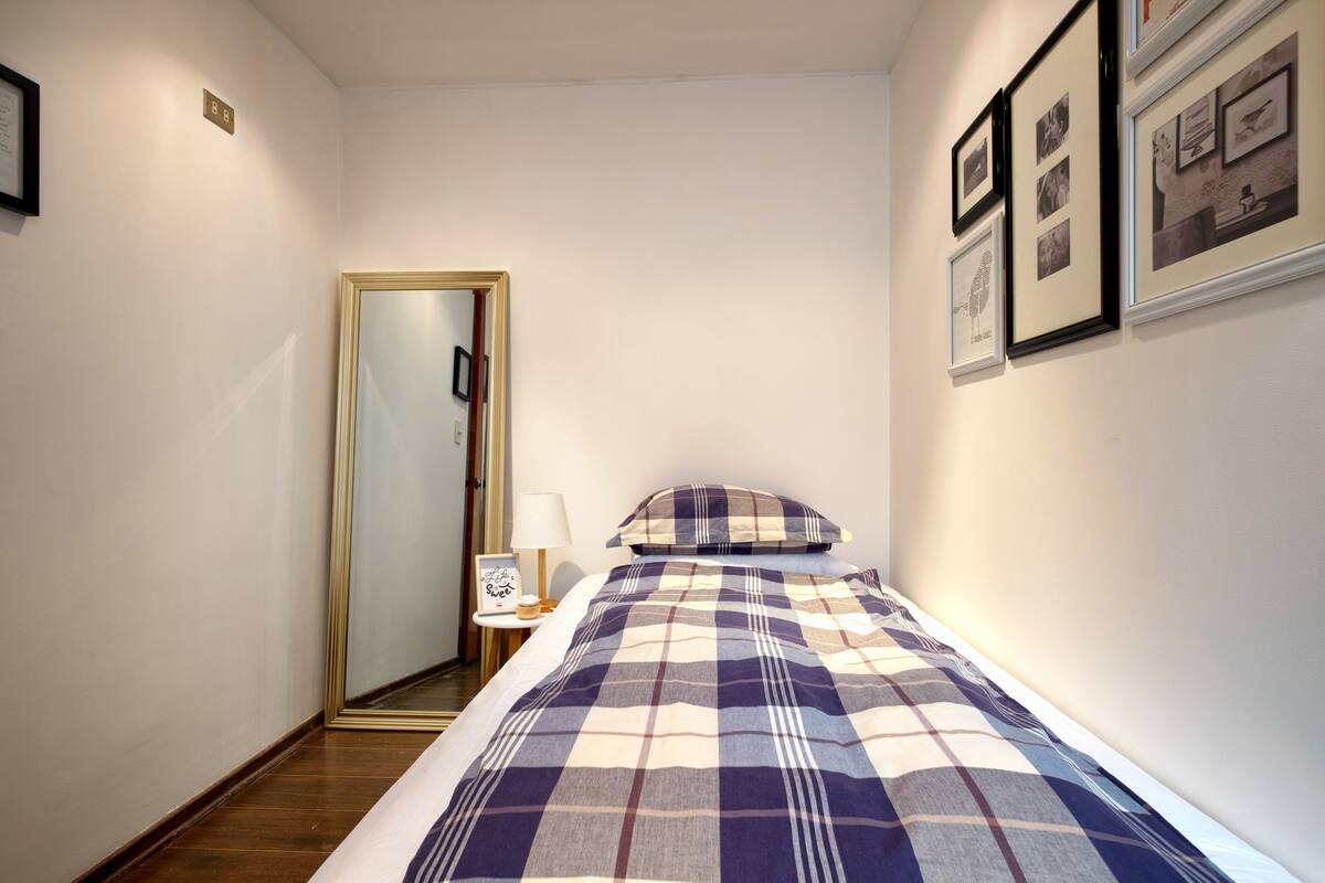 A bedroom with a bed, a bedside table with a lamp, a framed picture, and a mirror on the wall.