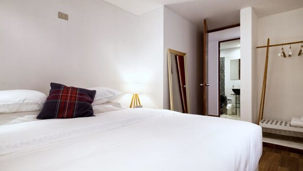 A hotel room with a large bed, a bedside table with a lamp, a wardrobe, and a bathroom visible through an open door. - InkaHuset Pacasmayo (Callao)