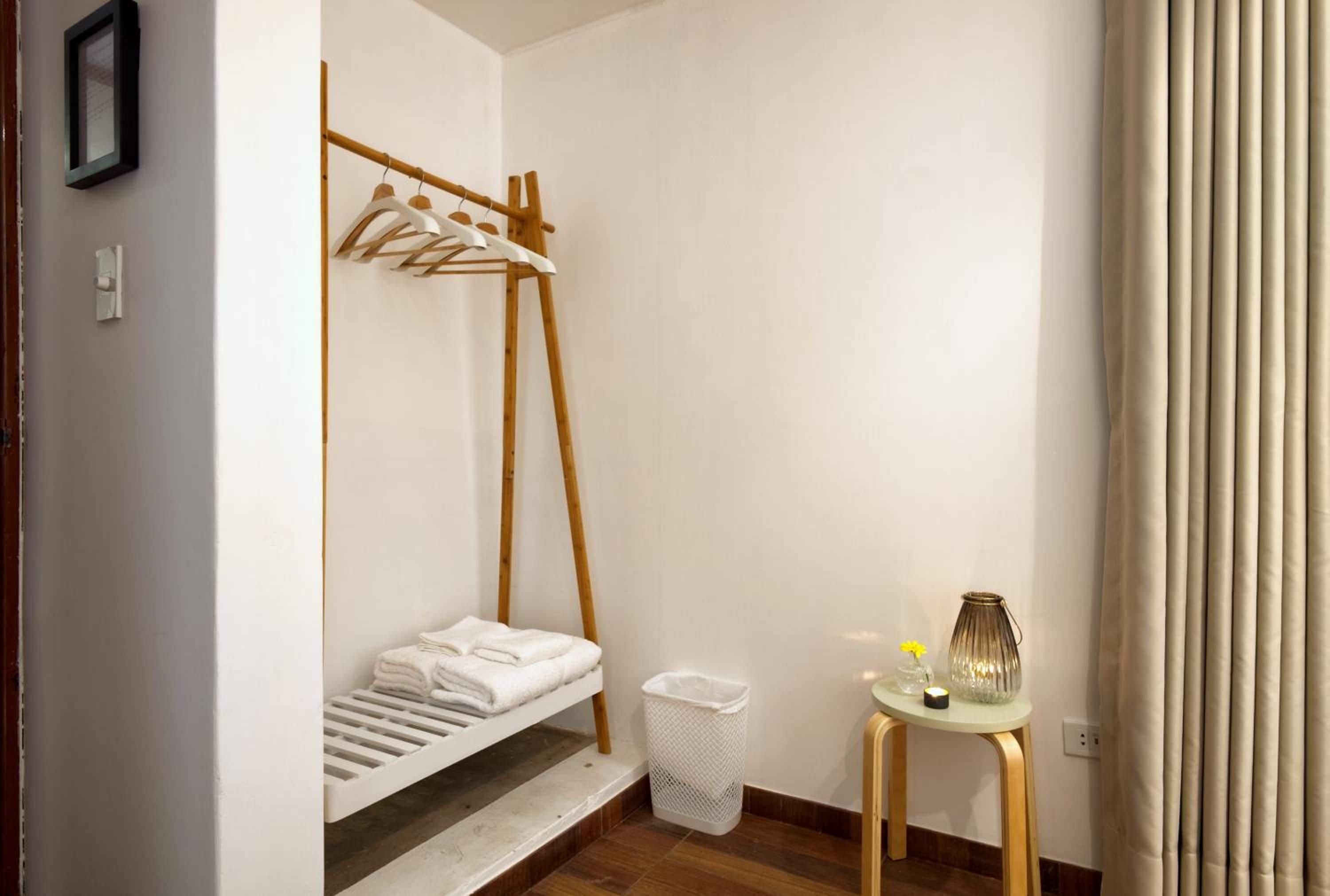 Quarto compacto com uma cama de solteiro, uma mesinha com luminária e um cesto de lixo.
