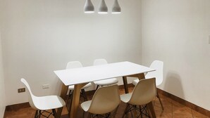 A dining area with a white table and chairs, a hanging light fixture, and a tiled floor. - InkaHuset Pacasmayo (Callao)