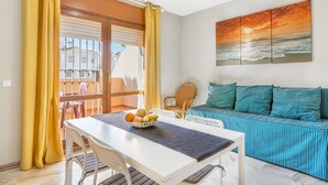 Una habitación con una mesa de comedor, un sofá, un cuadro de un atardecer y vistas a través de una ventana.