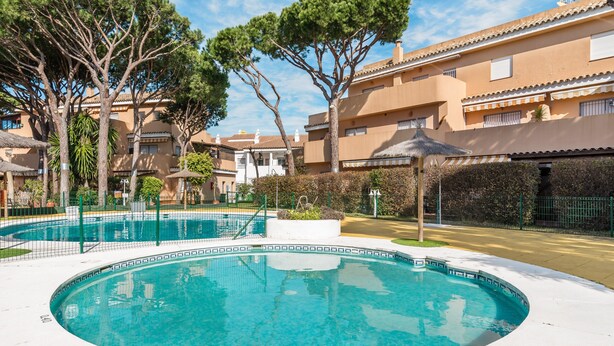 Una piscina rodeada por una valla, árboles y un edificio con techo de tejas.