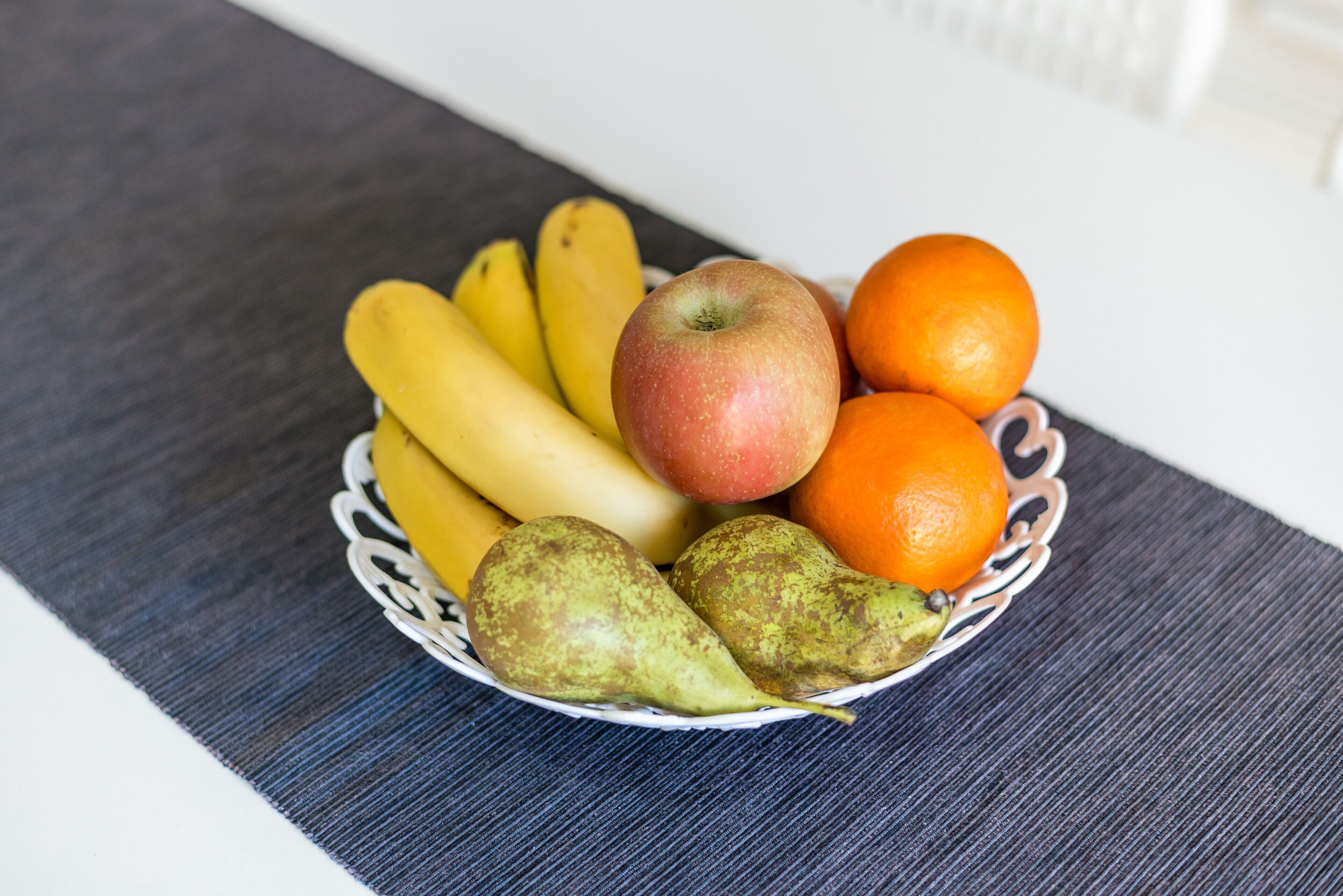 Una cesta de frutas con plátanos, manzanas, naranjas y peras sobre una mesa.