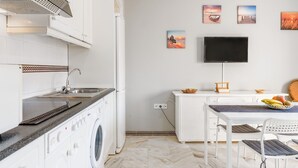 Una cocina funcional con lavadora, un comedor con mesa y sillas, y un televisor de pantalla plana montado en la pared.