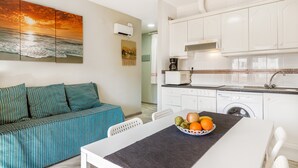 Una cocina moderna con armarios blancos, una mesa de comedor con fruteros, un sofá con cojines a rayas y un aire acondicionado de pared.