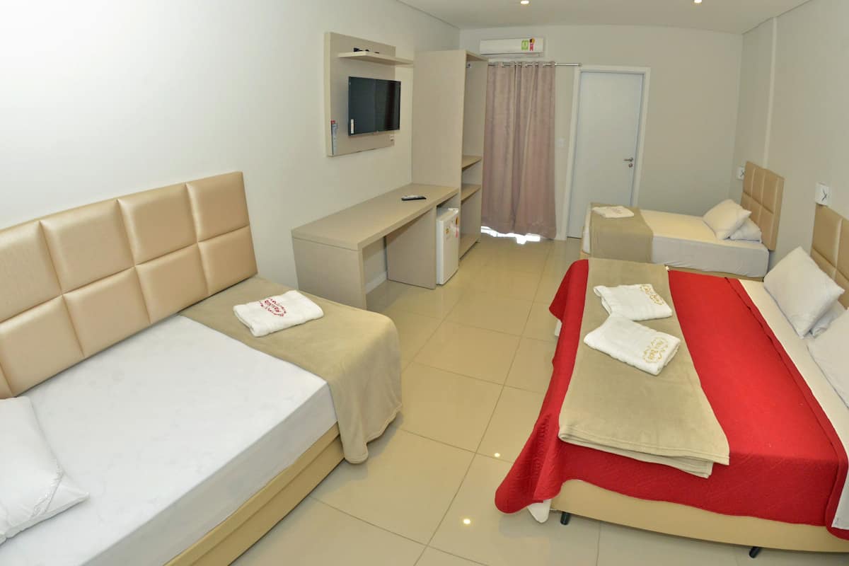 A hotel room with two beds, a desk, a TV, and a shower area.