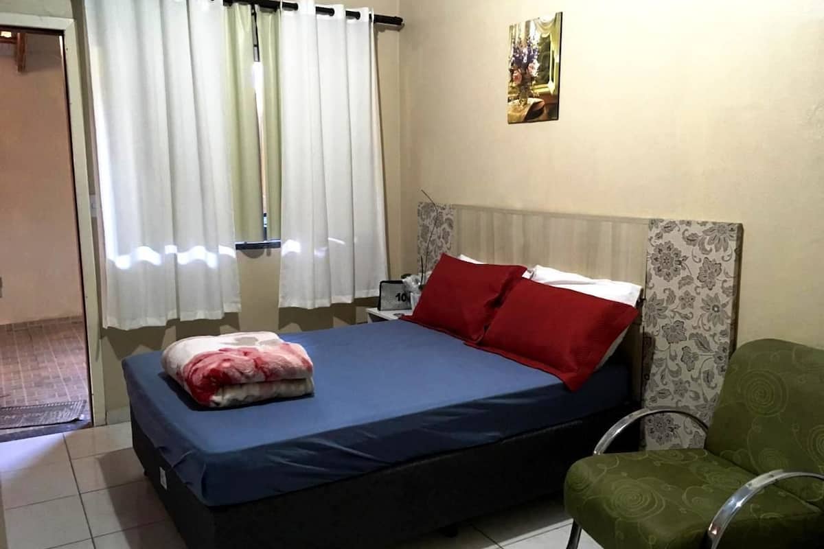 A bedroom with a bed, a chair, a nightstand, and a window with curtains.