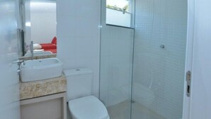 Un baño moderno con ducha envuelta en vidrio, lavamanos blanco y retrete.