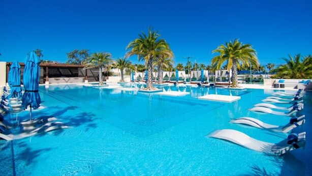A large swimming pool with multiple lanes, surrounded by palm trees and lounge chairs.