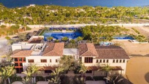 A resort with a swimming pool, palm trees, and a beach.