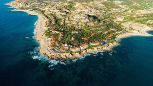 An aerial view of a coastal town with a beach, buildings, and surrounding hills.