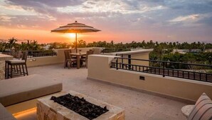 A rooftop terrace with outdoor seating, a fire pit, and a sunset view.
