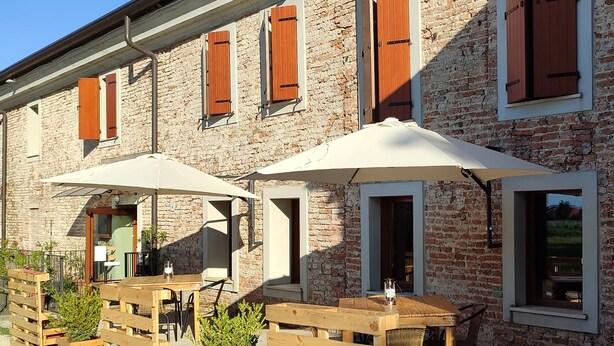 A rustic building with brick walls and wooden shutters, outdoor seating with tables and chairs, and planters with greenery. - Mulino Delle Valli (Casaleone)