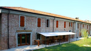 A brick building with a covered outdoor seating area and a grassy courtyard. - Mulino Delle Valli (Casaleone)