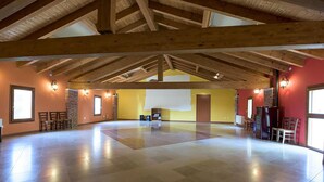 A spacious room with a high ceiling and exposed wooden beams, featuring a large open area with a projector screen, seating, and a fireplace. - Mulino Delle Valli (Casaleone)
