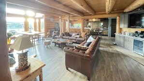 Tilava olohuone, jossa on suuri ruskea nahkasohva, puulattia sekä keittiöalue, jossa on televisio ja kaapistot.