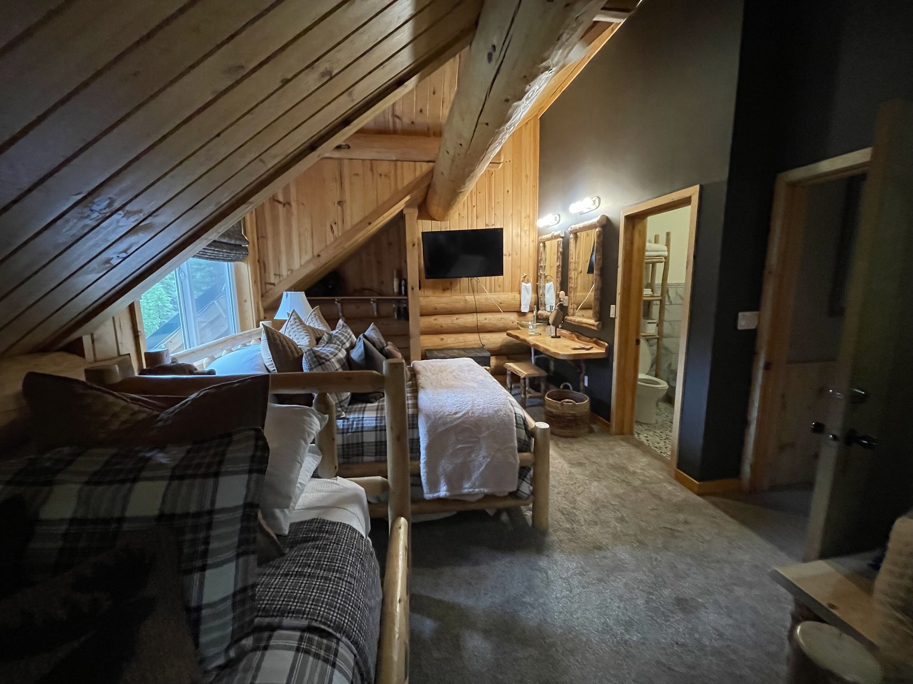 A cozy attic bedroom with a loft bed, a desk, and a mirror.