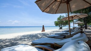 En strand med solstolar och parasoller, en sandstrand och en fri utsikt över havet.
