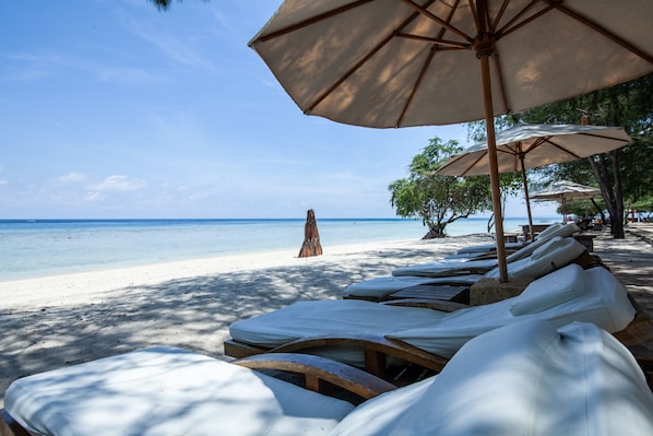 A beach with sun loungers and umbrellas, a sandy shore, and a clear view of the ocean.