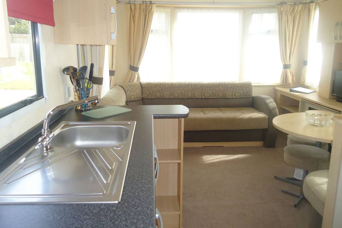 A compact RV kitchen with a sink, countertop, and a small dining area with a table and chair.
