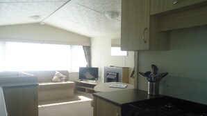 A compact RV interior with a kitchenette, a sofa, a television, and a dining area. - Mounts Bay Caravan Park (Marazion)