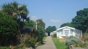 A caravan park with a paved path leading to a white caravan with a red sign. - Mounts Bay Caravan Park (Marazion)