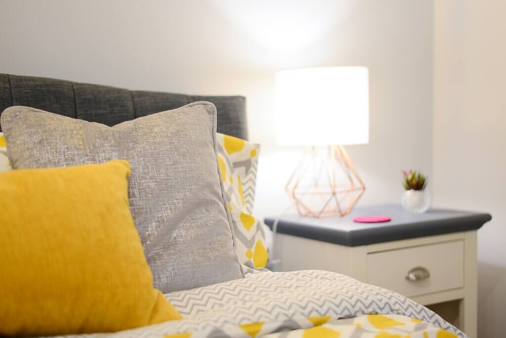 Een bed met beddengoed en kussens met een patroon, een nachtkastje met een lamp en een kleine plant.