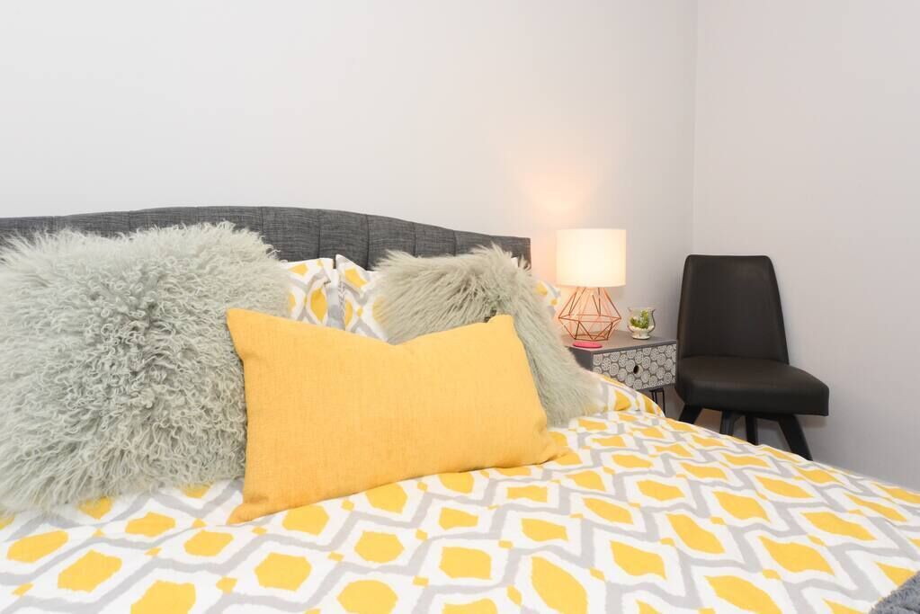 Una cama bien hecha con ropa de cama estampada, un plaid gris suave y una almohada amarillo mostaza.