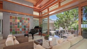 Un'ampia zona giorno con un pianoforte, posti a sedere confortevoli, una grande finestra vista giardino e elemento d'acqua.