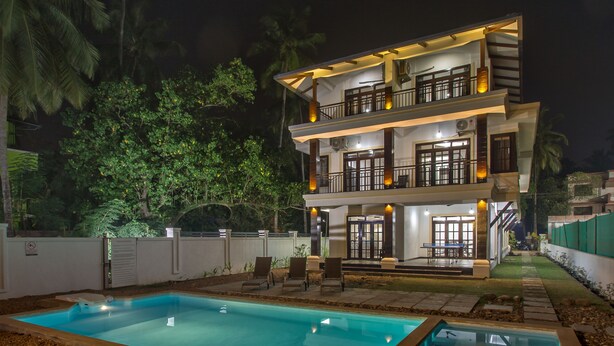 Una casa de dos pisos con piscina, mobiliario exterior y un balcón bien iluminado.
