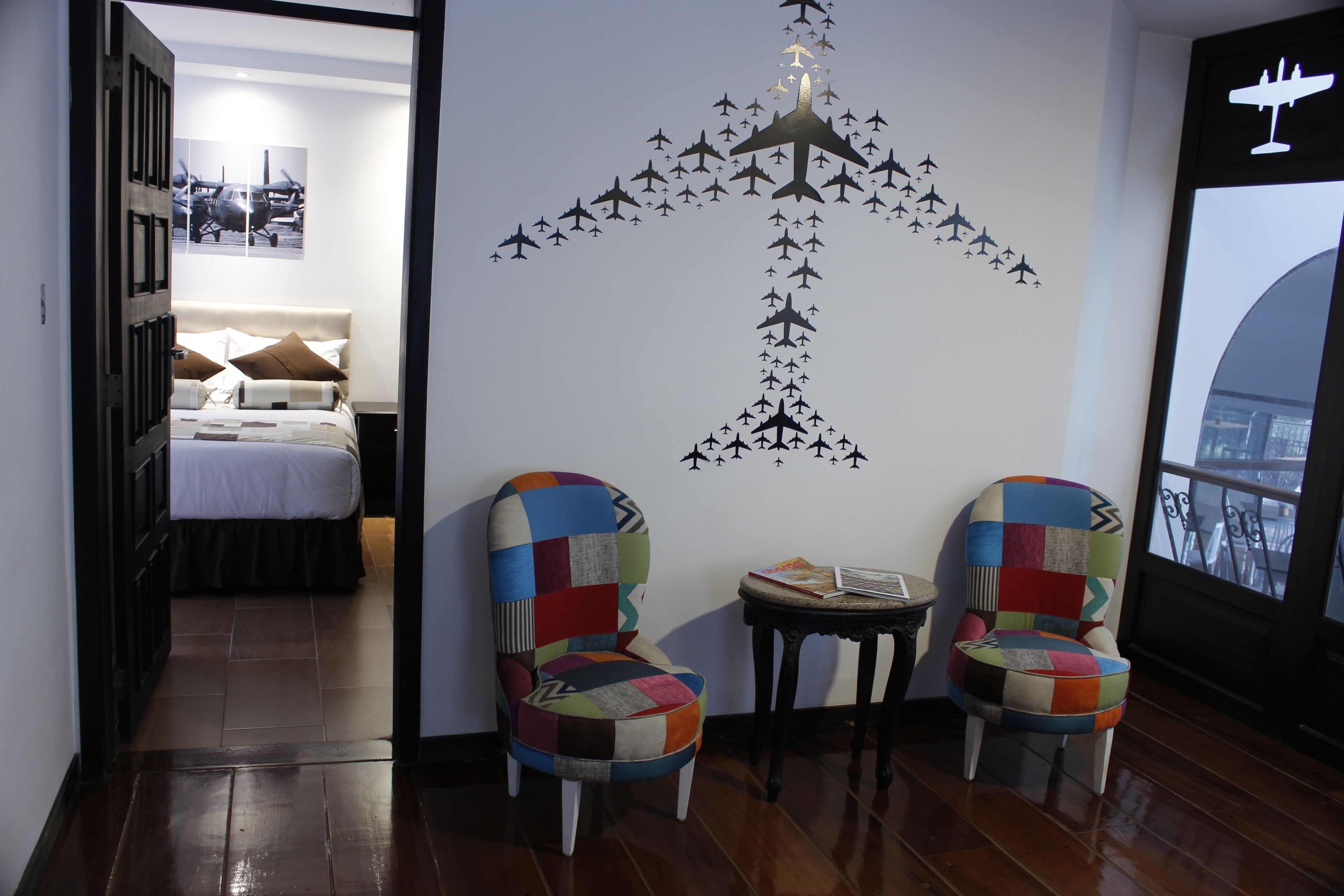 A hotel room with a bed, two colorful chairs, a small table, and a wall mural of airplanes.